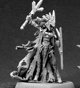 A female dark elf priestess attacking. She wears long anguar robes that are tattered and holed at their ends. Her headdress is a mass of vicious looking shards. In one hand she holds a V shaped shield close to her body. The other is held high behind her. In that hand she holds her tri forked weapon.