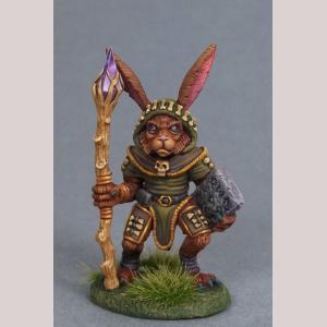 An anthropomorphic rabbit druid standing still. He is dressed in a simple robe and had a hood covering his head, In one hand he holds a rune inscribed stone tablet. His other hand holds onto the shaft of a large crystal topped staff.