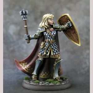A female human cleric standing defensively. She wears a knee length scale mail coat, leg greaves and shoulder pauldrons. Her back is covered with a full length flowing cloak. With one hand she holds a shield away from her body. The other holds an upright mace, ready to strike.