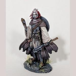 A female human cleric standing still. She wears a loose robe, overlaced with leather bag straps and belts. A long ragged cloak covers her back, and her round shield is strapped on top of that. In one hand she holds a small scroll case. The other hangs by her side, holding her mace.