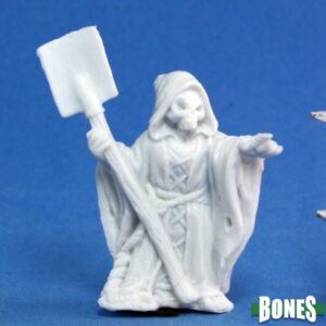 A small human undead skeleton wearing a hooded robe. In one hand he holds an upturned shovel while pointing with the other. Unpainted plastic RPG tabletop gaming miniature.